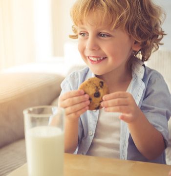 Niño desayunando un vaso de leche y una galleta